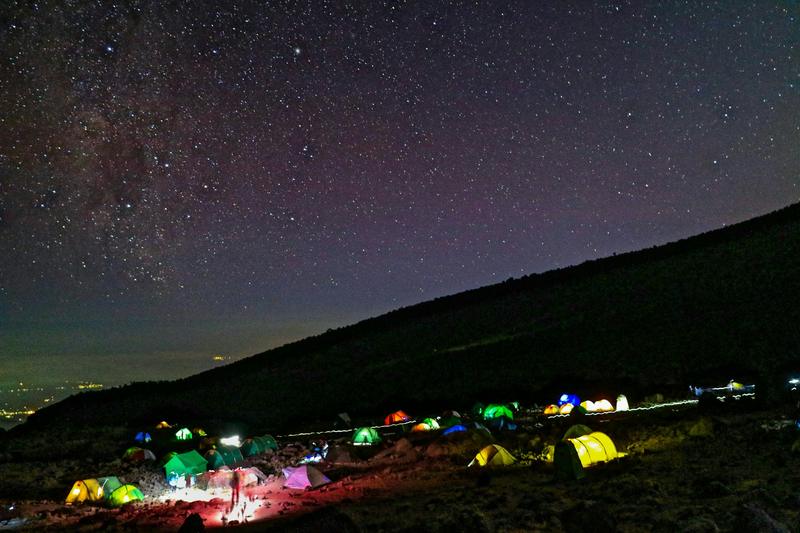 Lit-up tents of a high camp on Kilimanjaro under a starry night sky